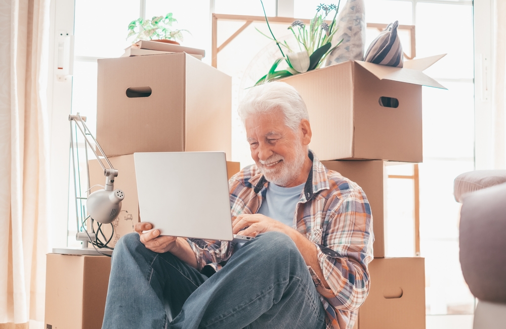 Senior man sitting on floor in front of many boxes, smiling